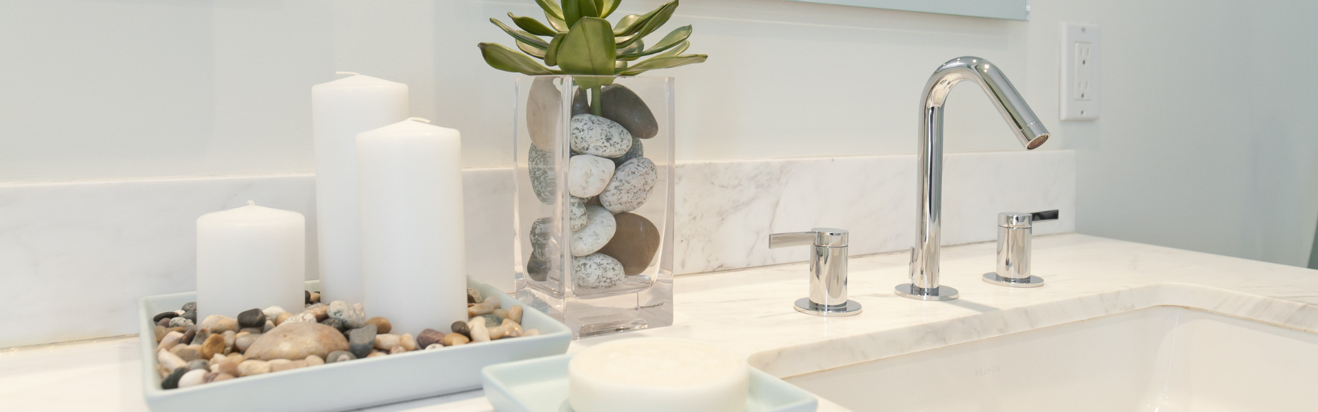 Marble vanity styled with candles and a small plant beside a chrome tap
