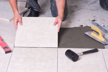 Tradesperson laying floor tiles with adhesive during a bathroom renovation