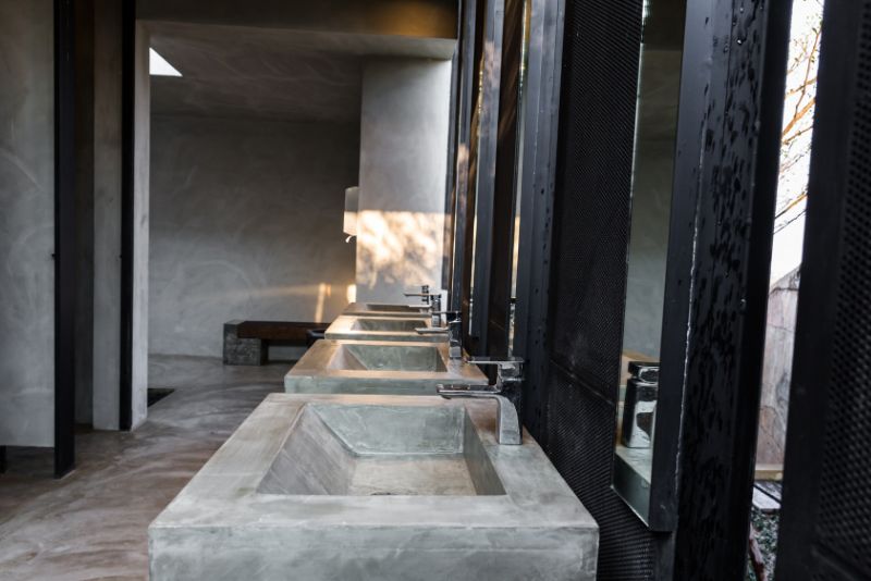 Concrete commercial washroom with a row of basins and privacy screening