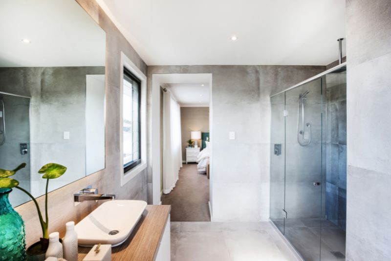 Ensuite bathroom with concrete-look tiling, glass shower and view through to the bedroom